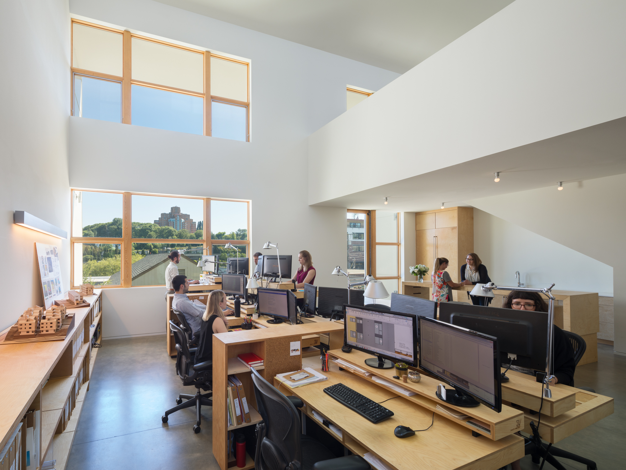 Open concept office featuring a combination of standing desks and sitting desks. Office has high ceilings and lots of windows with natural light.