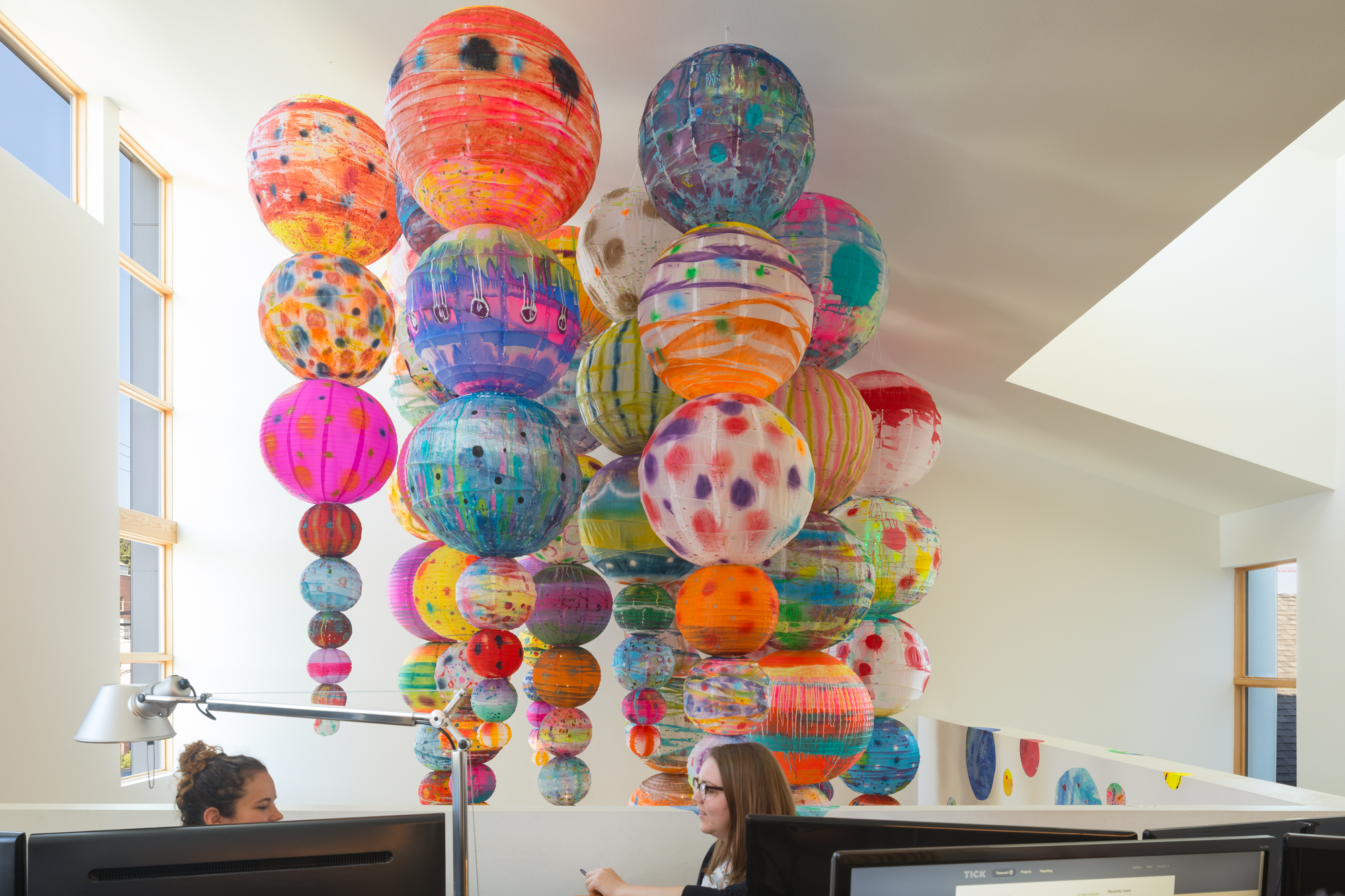 Office featuring hanging art installation of stacked spherical lanterns that have been painted bright colors and patterns.