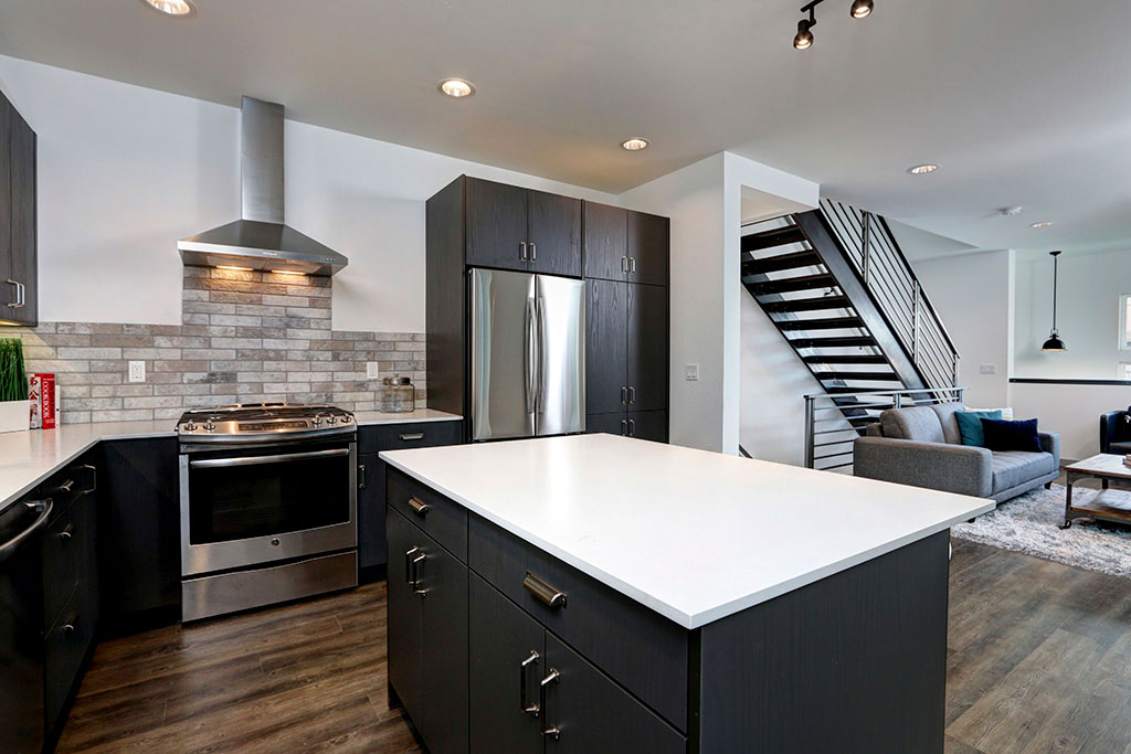 Modern kitchen with a black kitchen island and a white counter top, black cabinets, and silver fixtures