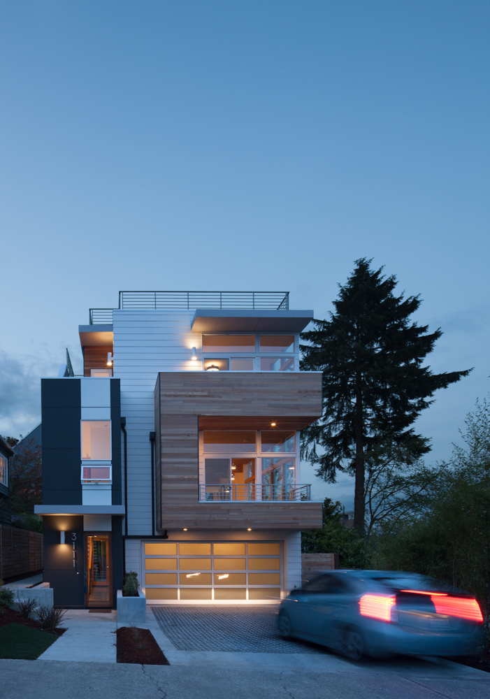 Exterior shot of single family home at night with a car driving into a garage below the home.