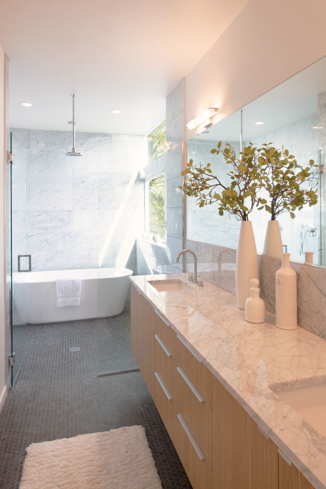 Bathroom with a marble counter top, and light wood cabinets, and white bathtub.