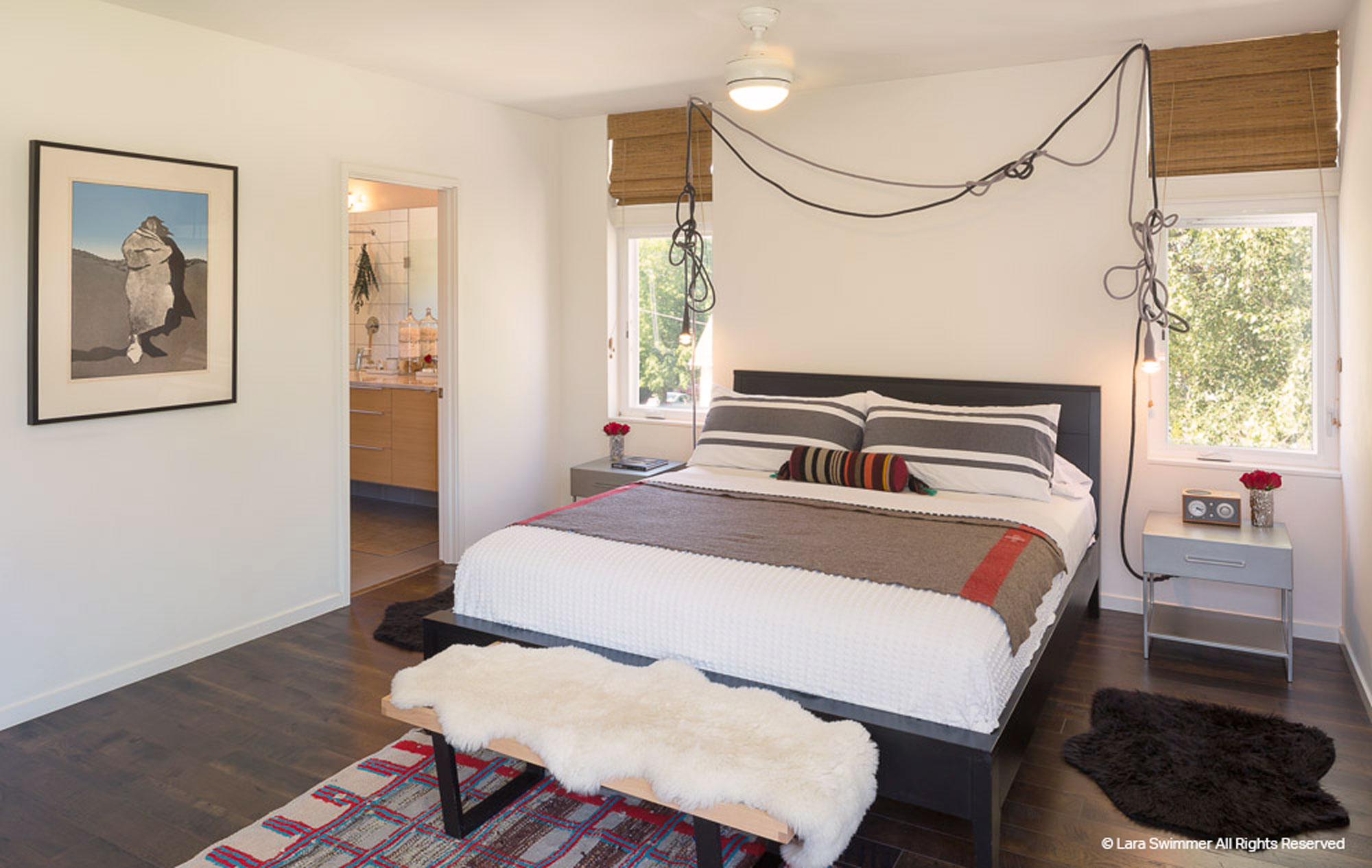 Bedroom with queen sized bed in the middle of the room. Two windows frame the bed.