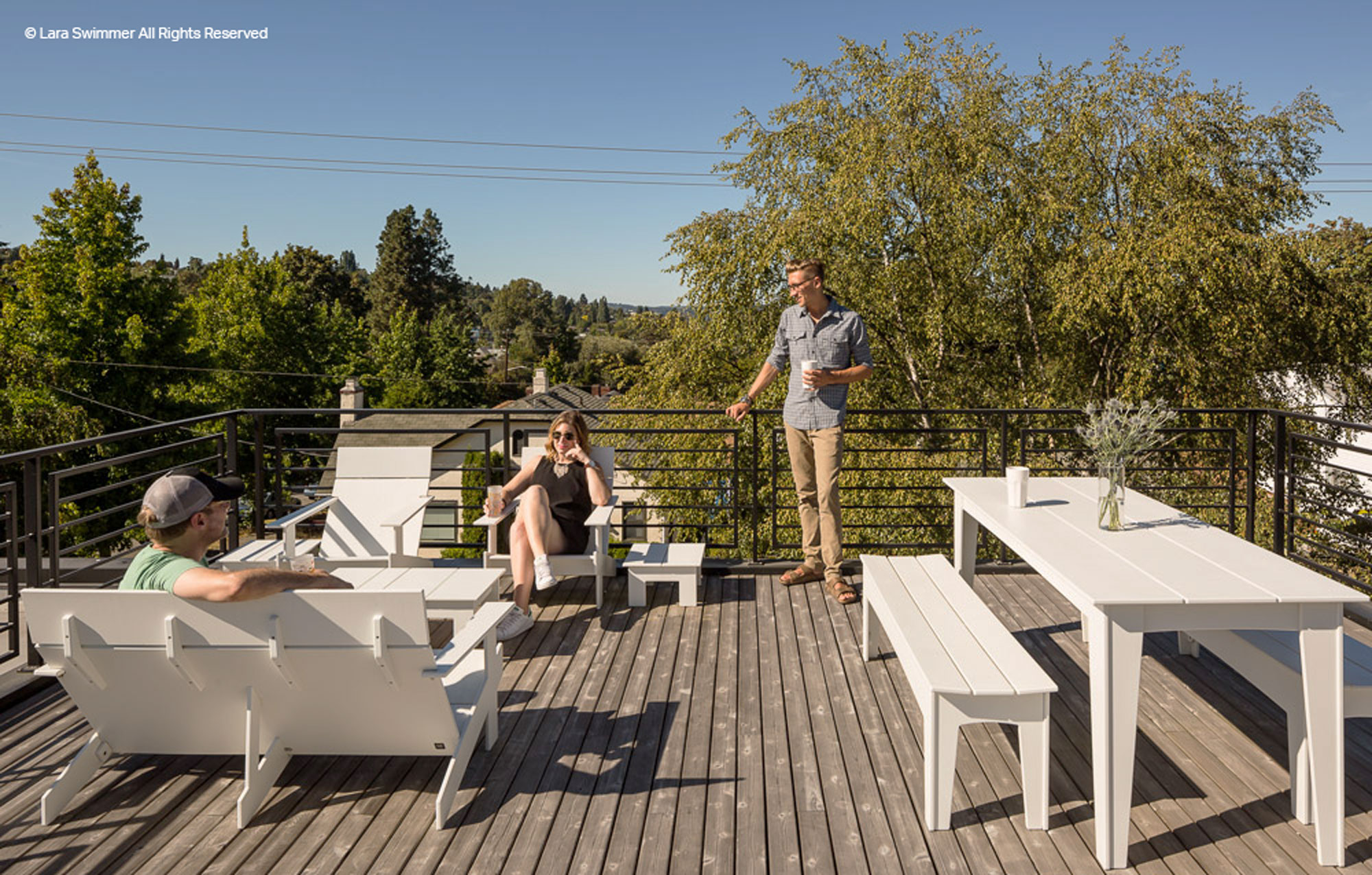 Rooftop deck with 3 people relaxing on outdoor furniture.