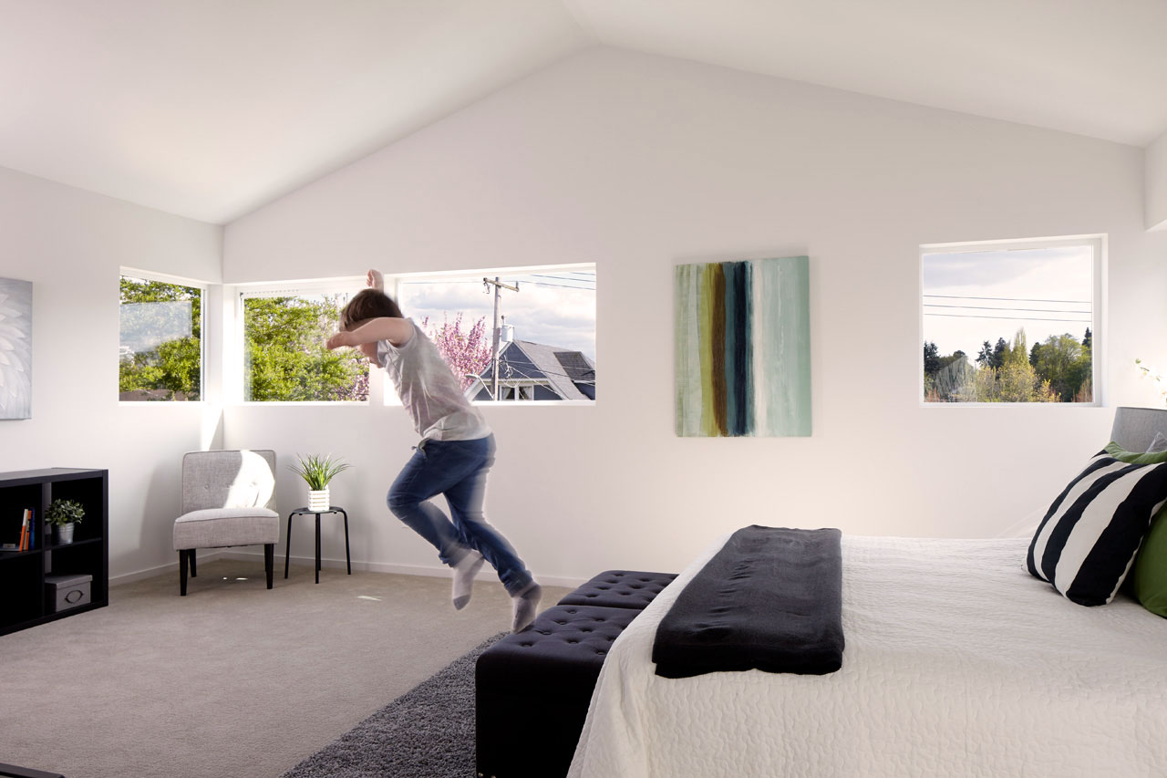 Child jumping off of a bed in a light filled bedroom